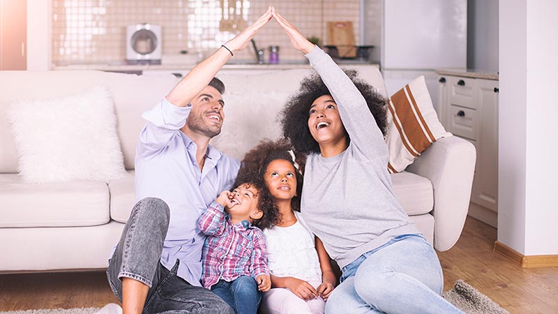 Family of four in living room making the shape of a house with their arms